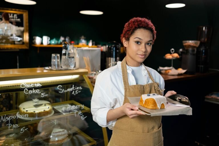 Young barista in a coffee shop holding a plate with a freshly served cake, ready to delight customers.